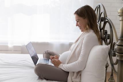 trudnica na laptopu sjedi na krevetu