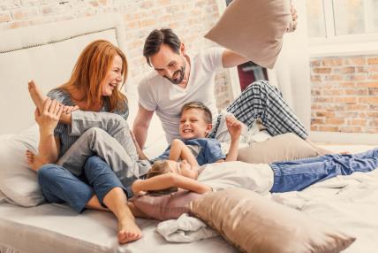 Mama i tata se na krevetu igraju jastucima s djecom